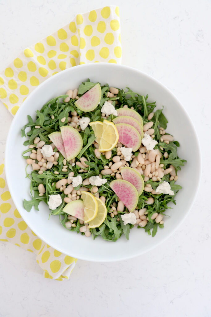 Large white bowl with arugula salad on top of a yellow napkin.
