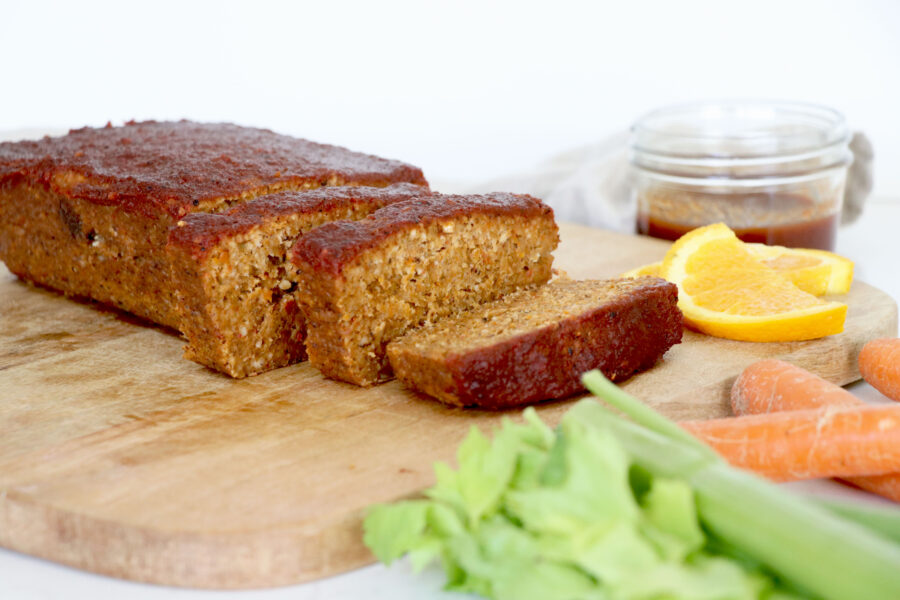 Lentil loaf cut on wooden board with celery, carrots and orange slice on the side.