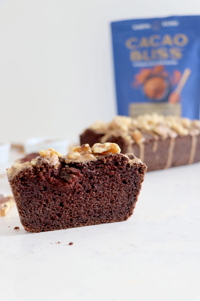 Slice of cocoa bread in front with loaf and cacao bliss package in background.