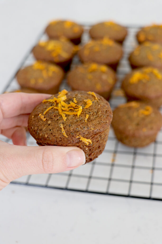 Muffins in a wire rack and hand holding muffin up front.