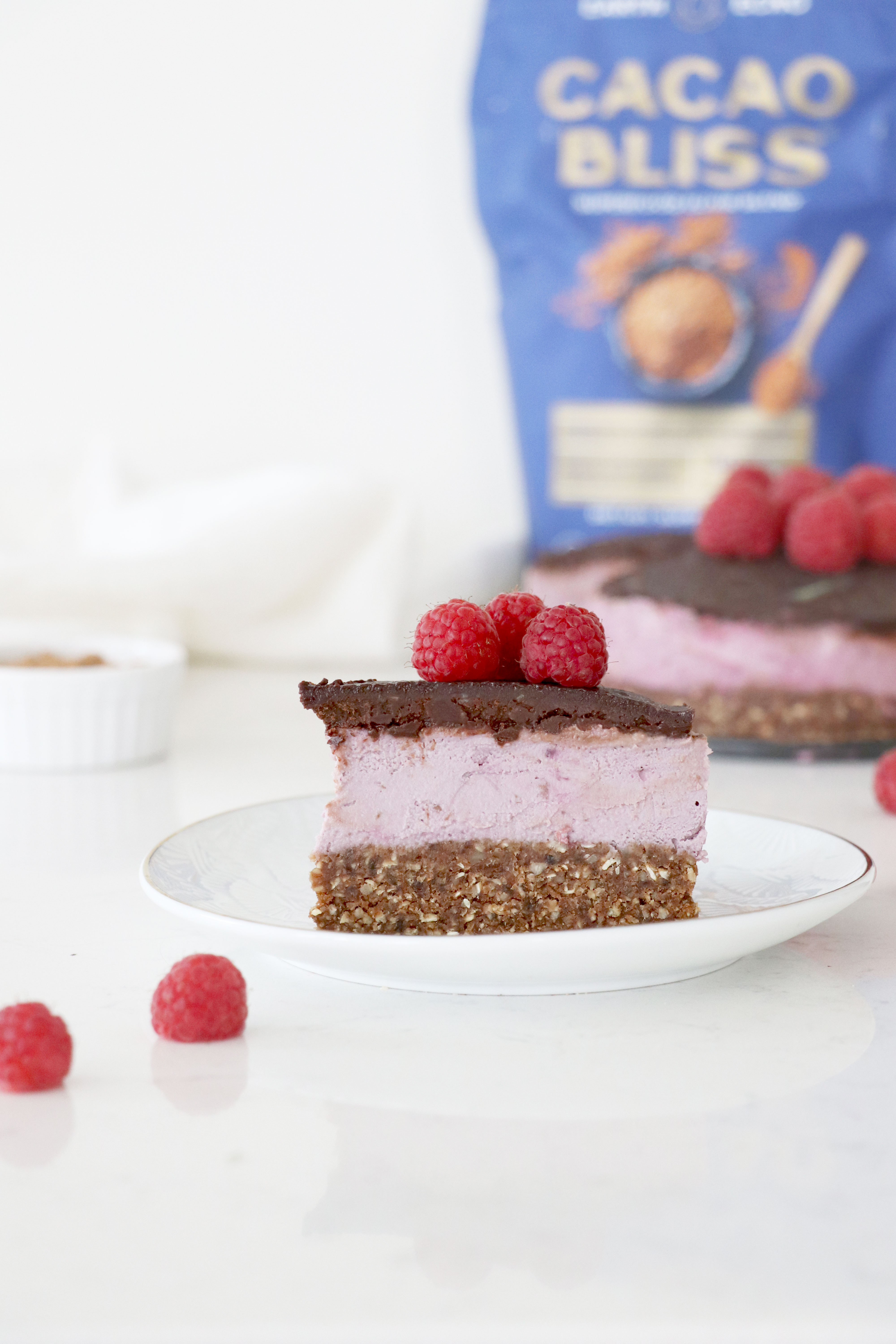 A slice of chocolate raspberry cheesecake with layers of chocolate crust, raspberry cashew middle, chocolate top layer and raspberries on top