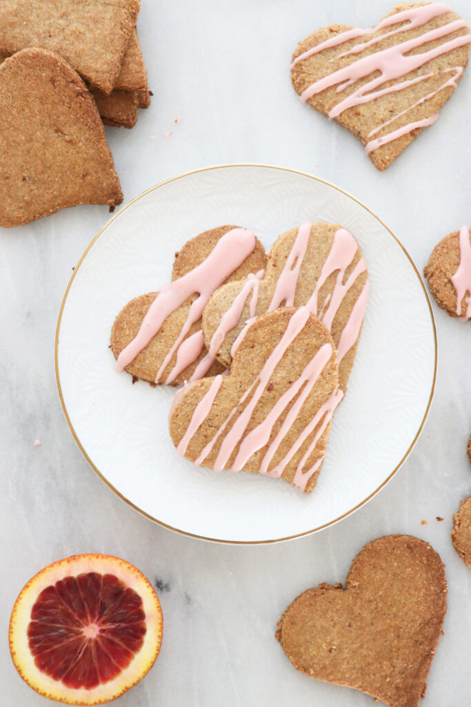 Heart shaped cookies with pink icing on top. Slice of blood orange in background.