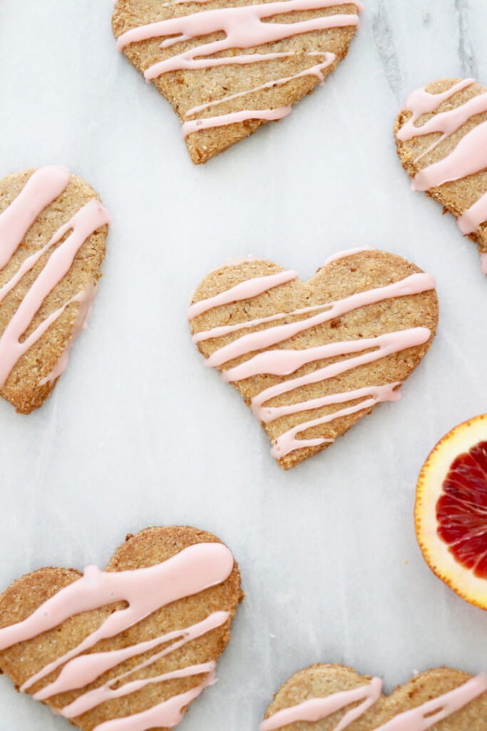 Heart shaped cookies with pink icing on top. Slice of blood orange in background.