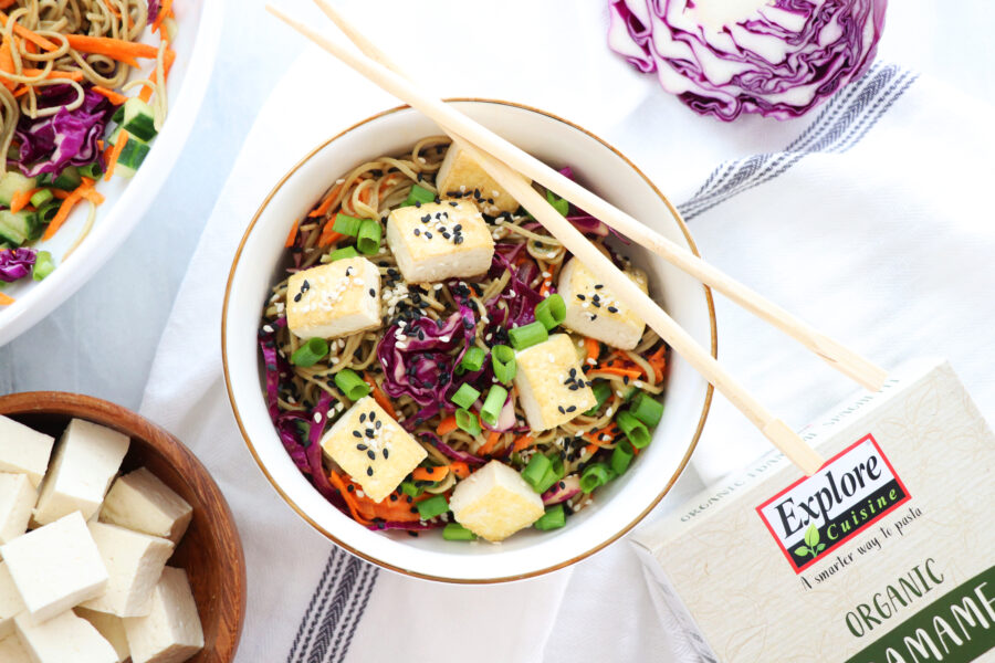 Edamame Spaghetti in a bowl with tofu, black sesame seeds, purple cabbage, shredded carrots and green onion
