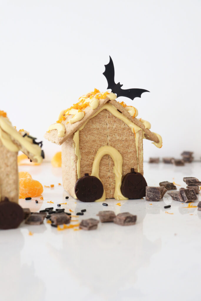 Edible spooky houses made from graham crackers, frosting, orange pumpkins and decorated with a bat on top.