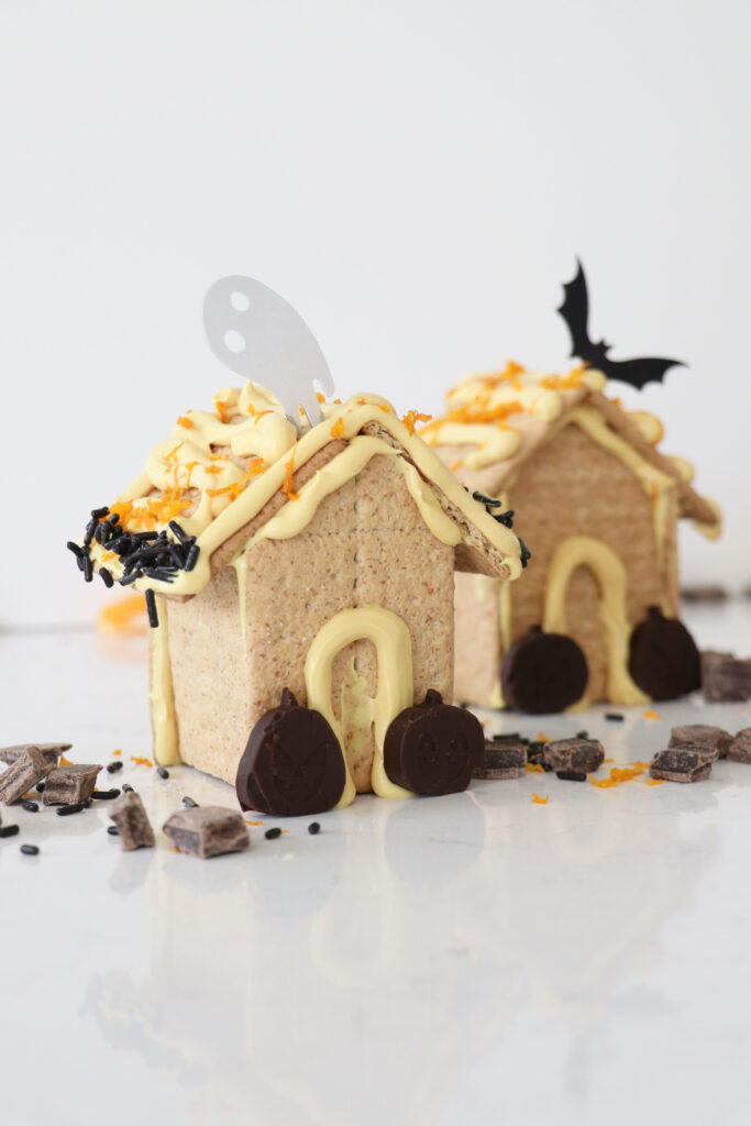Two spooky graham cracker houses with chocolate pumpkins, orange frosting and decorative candy.