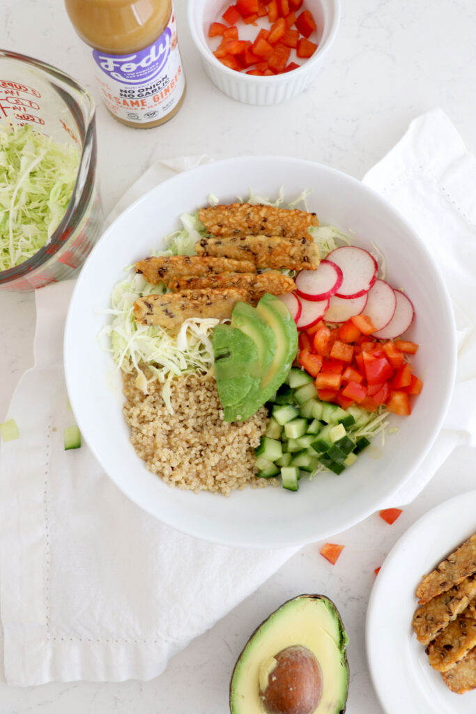 White bowl with low fodmap ingredients. Surrounded by Fody dressing and sliced veggies.