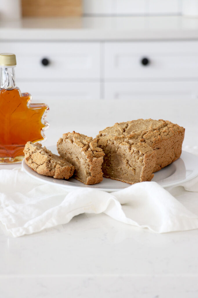 Vertical photo with gingerbread loaf on white plate and napkin. Syrup on left side.