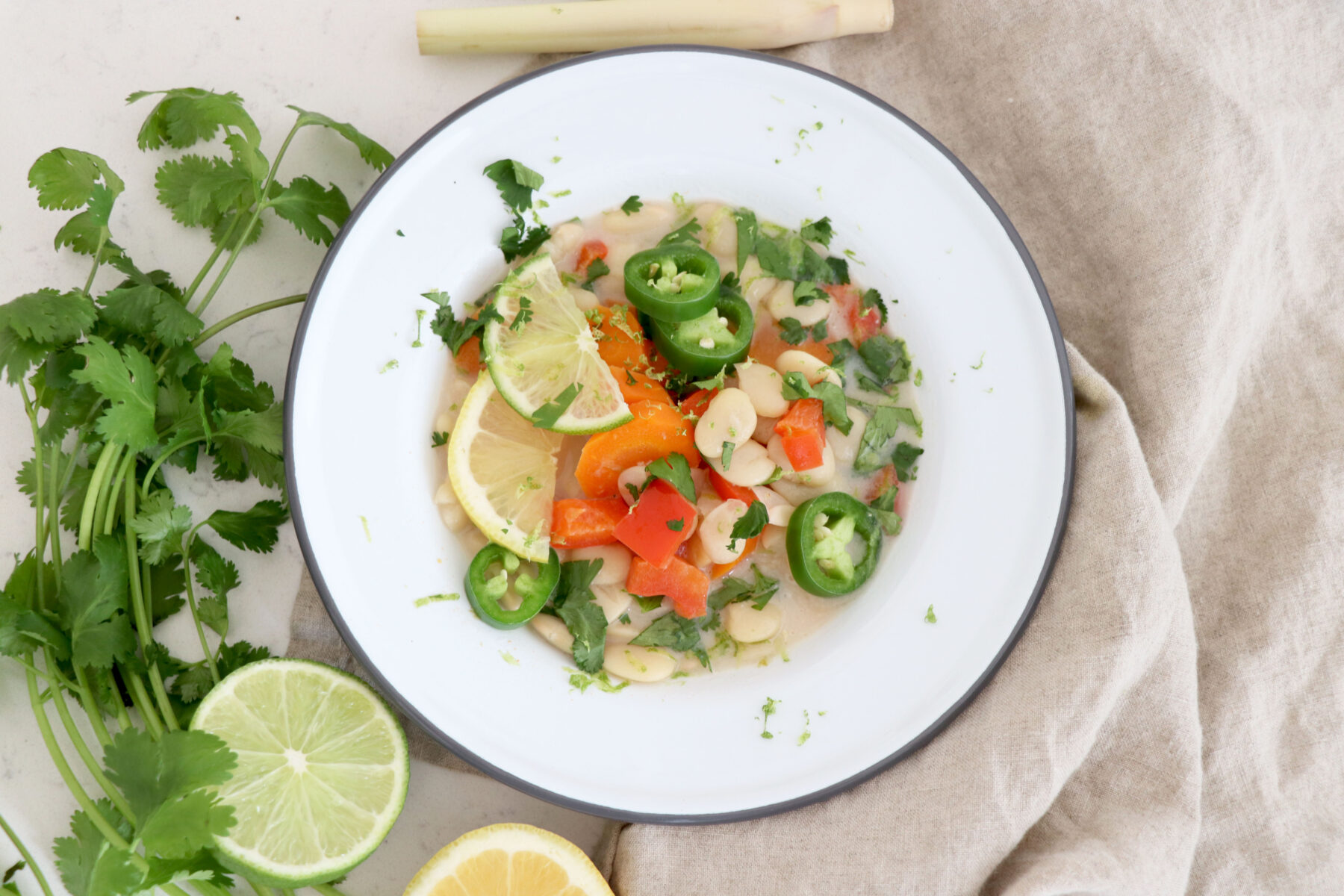 plate bowl with butter bean soup and cilantro with citrus slices on the left side.