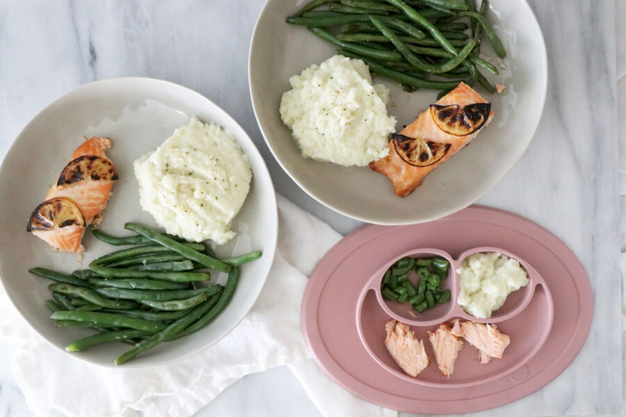Two white plates and one pink children's plate with salmon, mashed cauliflower potatoes and green beans.
