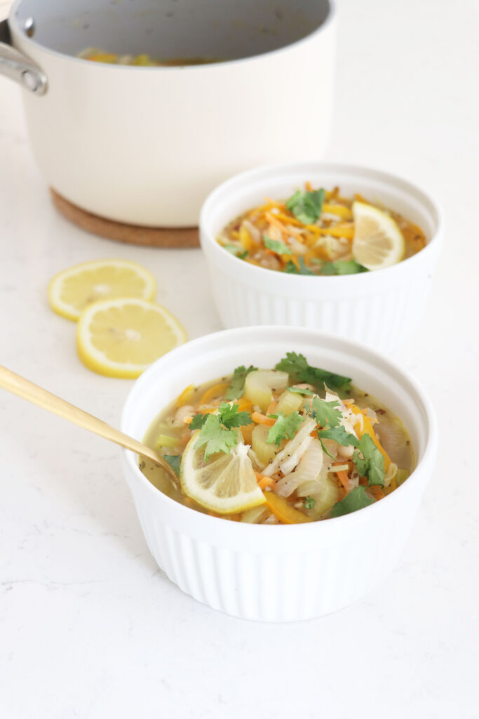 Two white bowls of cabbage soup with pot in the background.