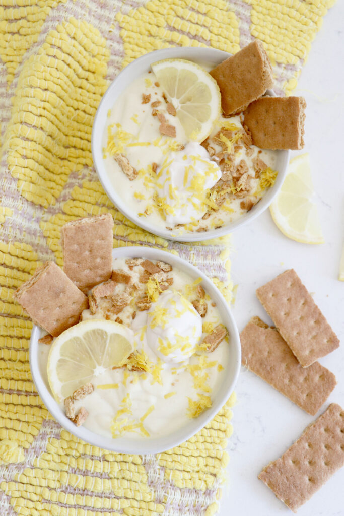 Two white bowls with smoothie topped with lemon slices, graham crackers and lemon zest. Lemon slices and grahams on the side.