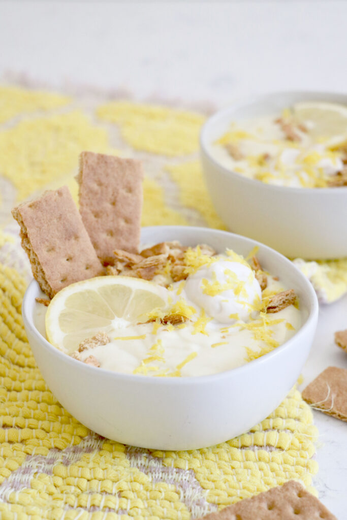 White bowl of meringue pie smoothie. Graham cracker sticks on the side with lemon zest and a lemon slice on top.