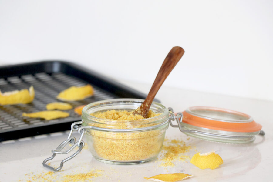 Clear storage container with lemon peel powder and a wooden spoon on top.