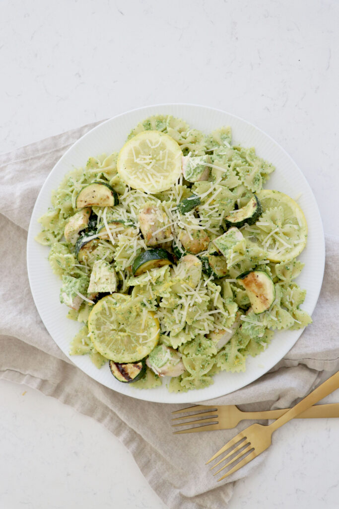 White bowl with pesto pasta with chicken, zucchini and lemon.