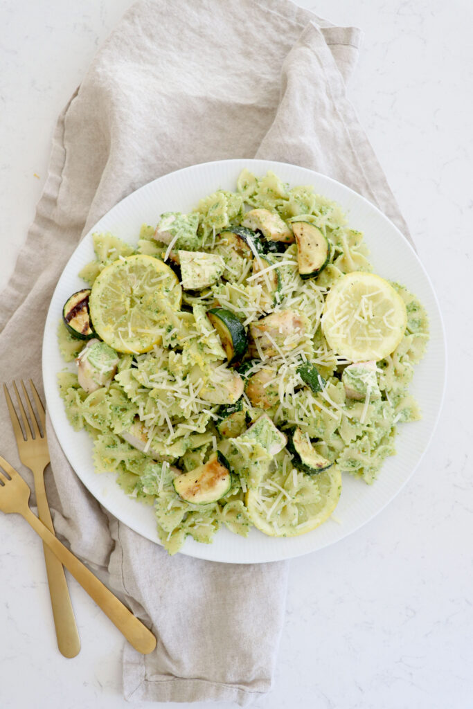 White plate with pesto pasta and utensils on the side.