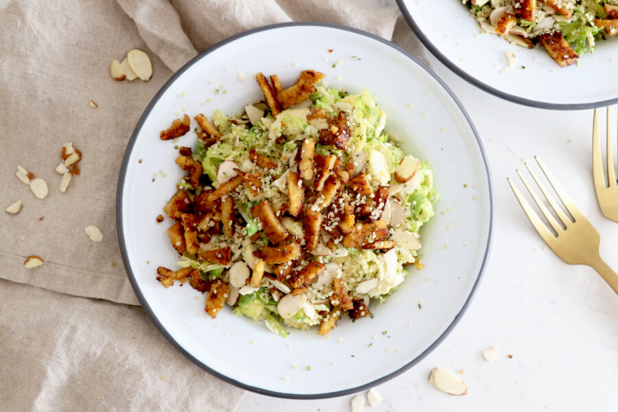 White plate with maple tempeh bacon Brussel salad with another plate and forks off to the side.