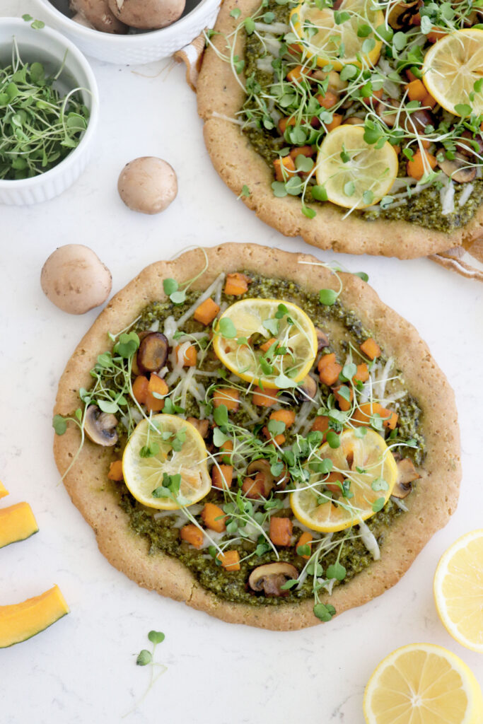 2 pizzas with roasted veggies, roasted lemons and sprouts on top.