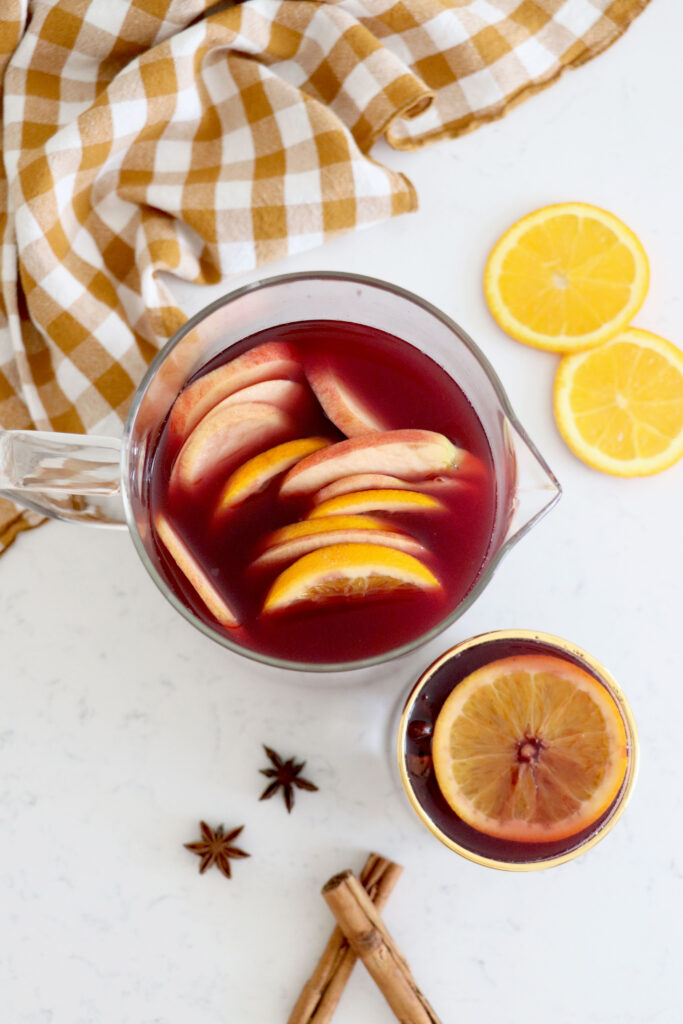 Glass pitcher with sangrias and orange and apple slices on top. Orange slices on the side.
