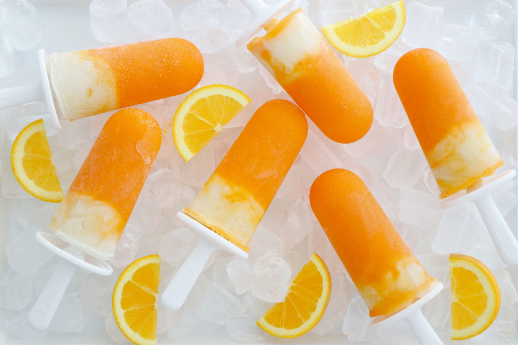 Creamsicle popsicles with orange and orange slices all on ice.