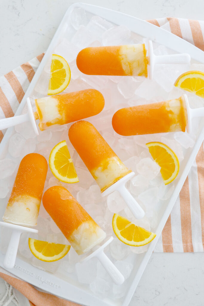 Orange creamsicle popsicles on ice with orange slices around them.