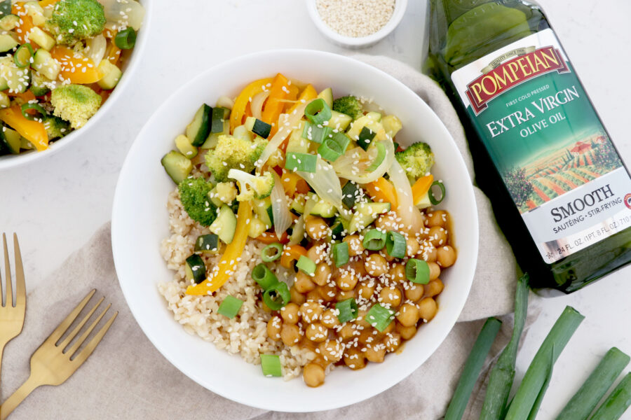 White bowl with orange chickpea stir fry with olive oil on the right side.