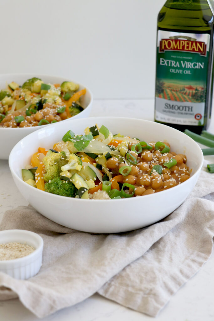 Bowls of stir fry topped with green onions and bottle of olive oil on the side.