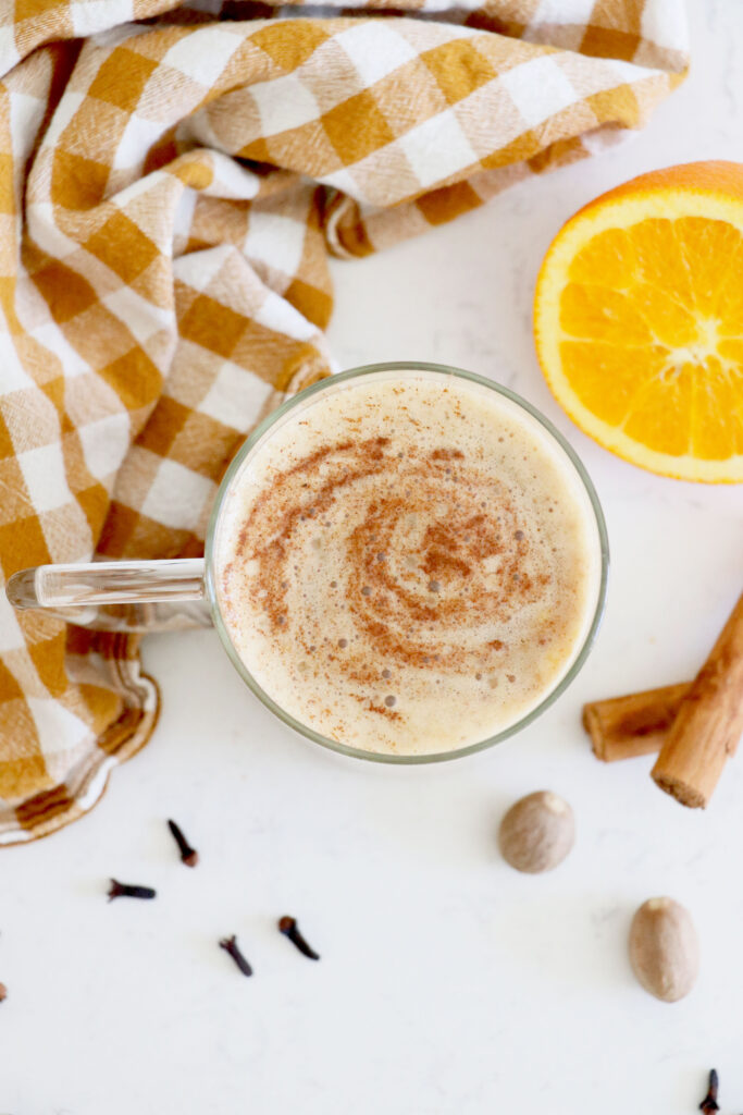 Birds eye view of coffee mug with latte and orange slice, cinnamon sticks and napkin around mug.