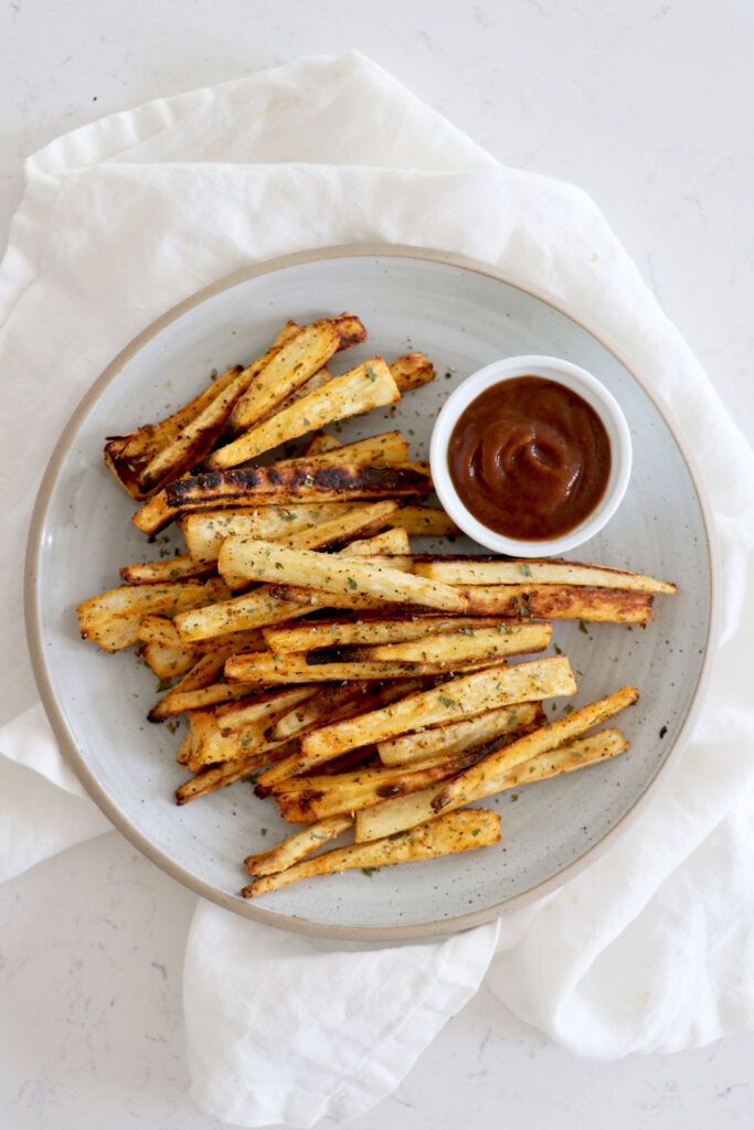 Parsnip fries on white plate with a small dish of ketchup