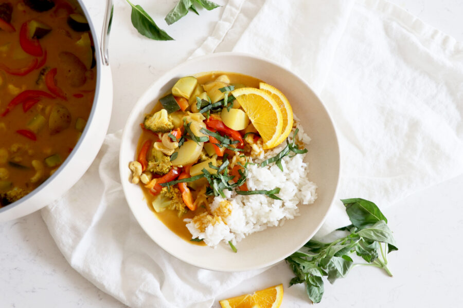 White bowl with veggie curry, rice and surrounded by soup pot.