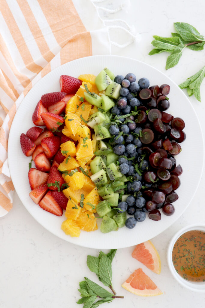 White plate with fruit in rainbow color order on top of a towel.