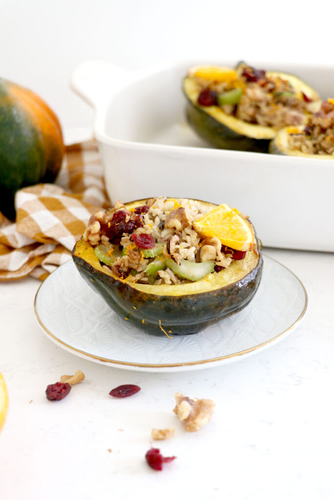 White plate with stuffed acorn squash and baking dish in the background.